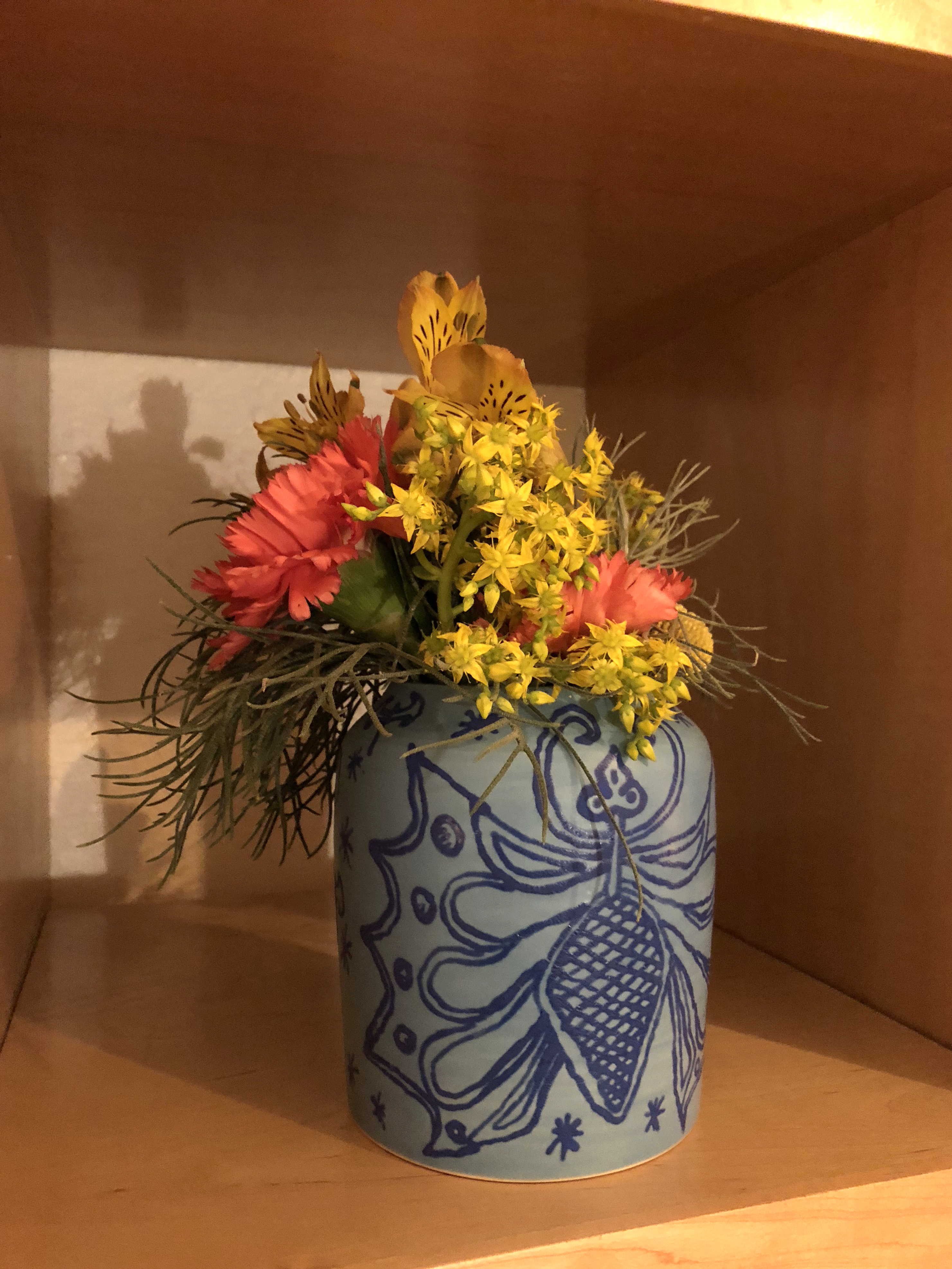 Blue ceramic vase with drawings on it holding colorful flowers